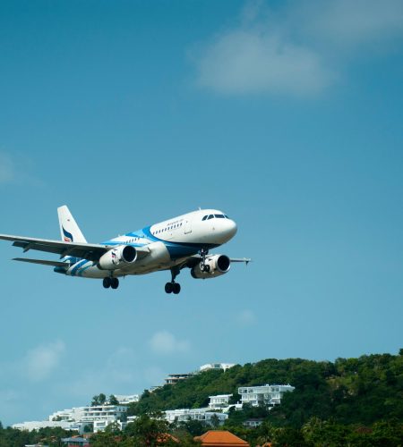 A passenger airplane descends for landing over lush hills in sunny Thailand.
