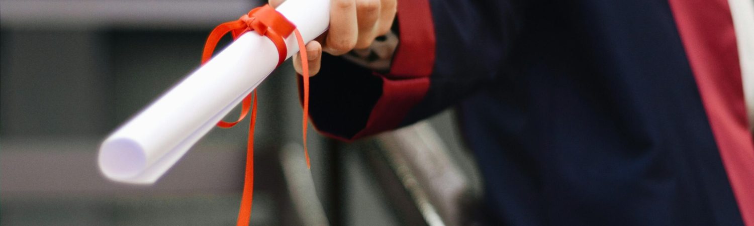 A close-up image of a graduate holding a diploma tied with a red ribbon, symbolizing achievement and success.